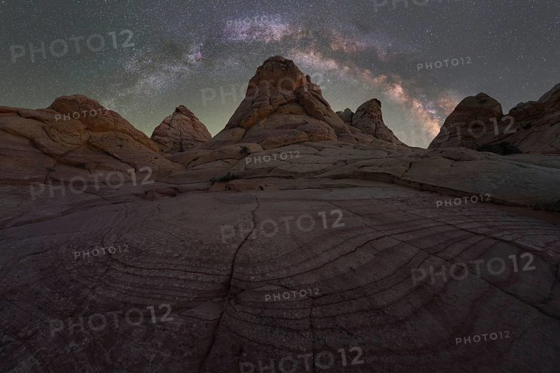 A breathtaking night sky view featuring the Milky Way over textured rock formations in the Utah desert, creating a stark and beautiful contrast