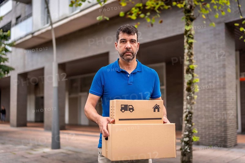 Serious mature male caucasian messenger carrying box while walking in city