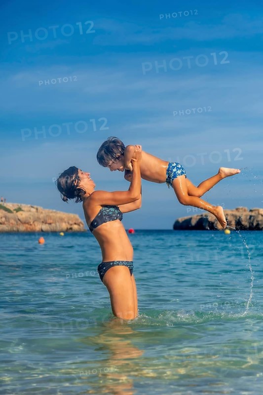 A woman is holding a child in the ocean. The child is wearing a blue and white bathing suit