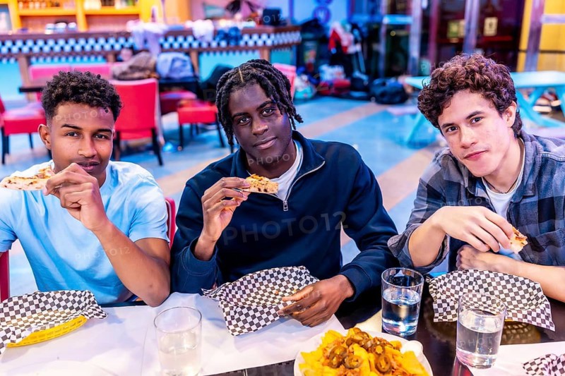 Diverse group of young male friends enjoying pizza and nachos at a bowling alley restaurant, sharing good times and delicious food