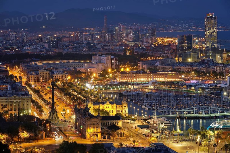 Aerial view of Barcelona city skyline with city traffic and port with yachts illuminated in the night. Barcelona, Spain