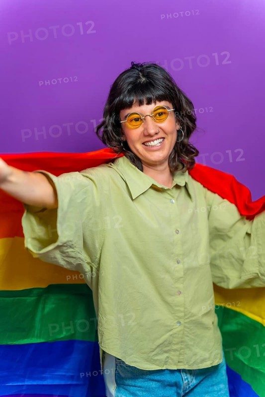 Studio portrait with purple background of a happy non binary person raising lgbt rainbow flag