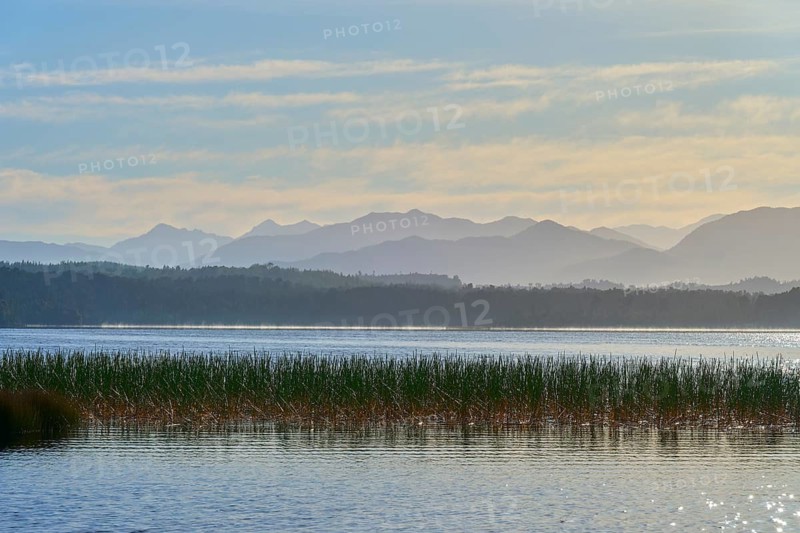 Lake against a mountainous backdrop and cloudy sky, Lake Mahinapua, Ruatapu, South Island, New Zealand