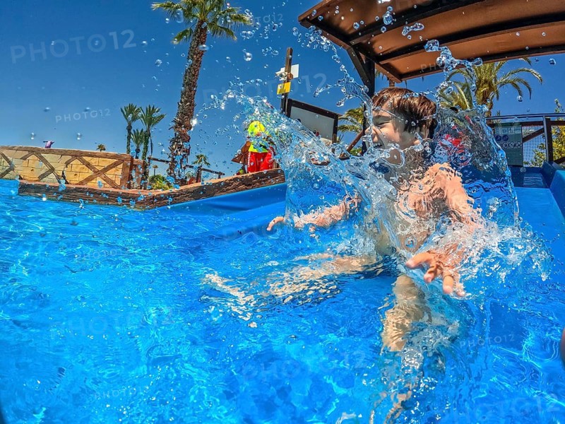 Young boy enjoying summer vacation splashing in a swimming pool at a water park, creating a refreshing spray of water