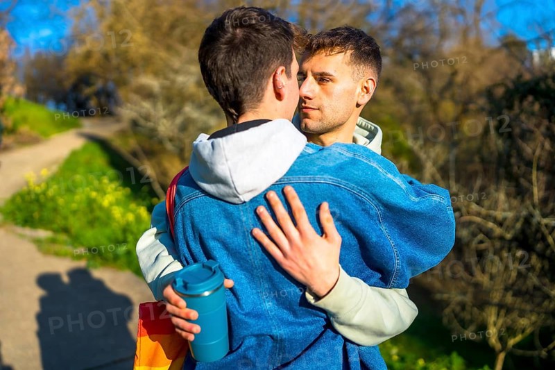 Two young men embracing tenderly in a park, showcasing their love and affection for one another under the warm sunlight of spring