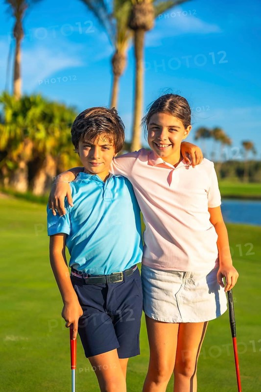 Vertical portrait of caucasian young sister and brother embracing and smiling in a green golf course