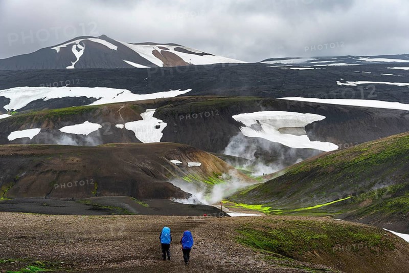 Hikers in dramatic volcanic landscape with mountains and snow, volcanic steaming hot springs, trekking trail Laugavegur, Landmannalaugar, Fjallabak Nature Reserve, Icelandic Highlands, Suðurland, Iceland