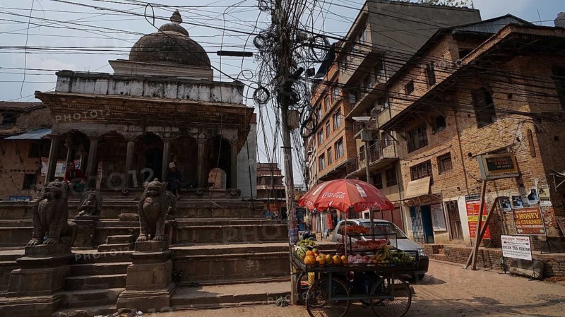 Street scene with a sales stand and a tangle of electrical cables in front of an old temple in Kathmandu, Nepal