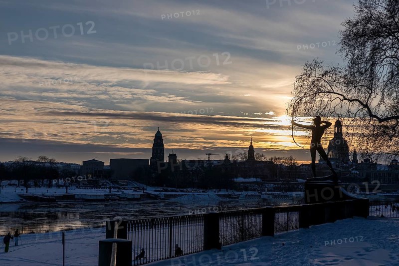 Bronze figure The archer in the snow, in the background the Elbe with drift ice and the old town with Church of Our Lady in the evening light, Dresden, Saxony, Germany