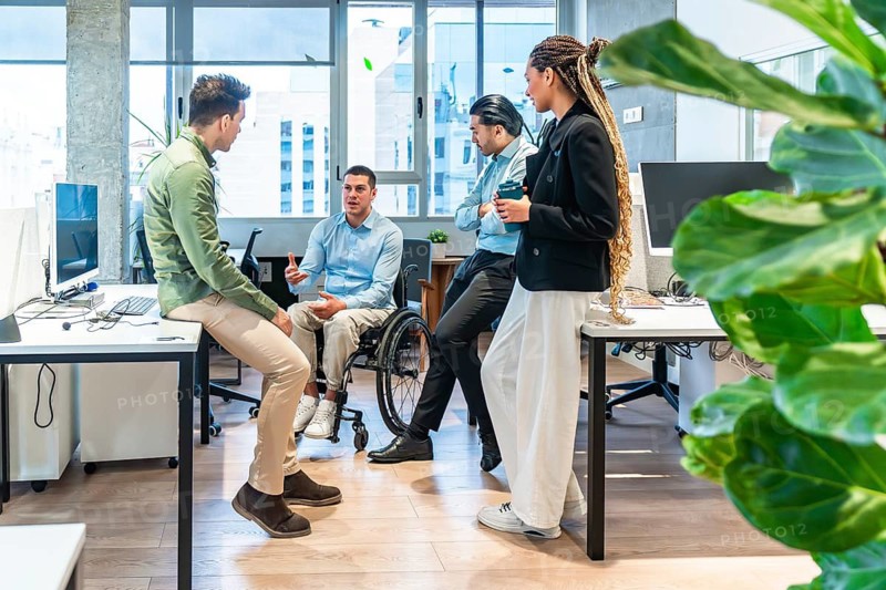 Business team having a discussion in a modern office, including a colleague using a wheelchair, showcasing workplace diversity and inclusion
