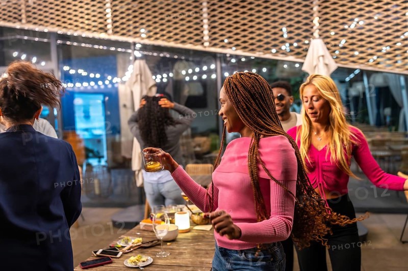Multi-ethnic playful friends dancing around a table during night party in the terrace of a bar