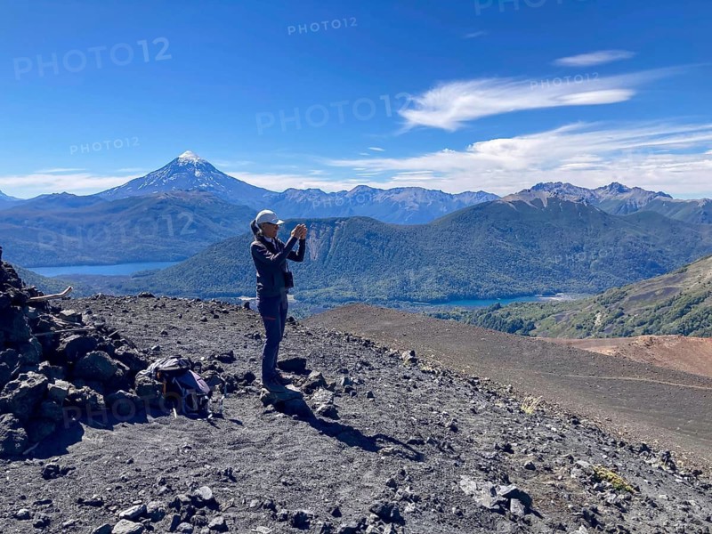 Woman taking a photo with her mobile phone of the view from the summit of the Achen Niyeu volcano in Lanin National Park, Patagonia, Argentina