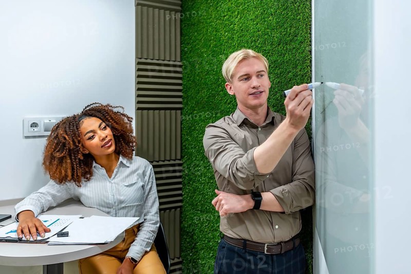 Two business colleagues collaborating, developing innovative strategies, writing on a whiteboard in a modern coworking office