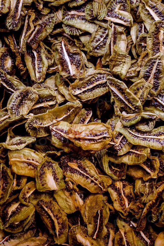 Close up image showcasing numerous dried kiwi slices, highlighting their intricate texture and vibrant greenish brown hues, capturing a natural and healthy snack option