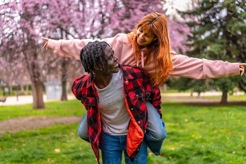 Interracial couple having fun together outdoors in a park during springtime with pink flowers blooming