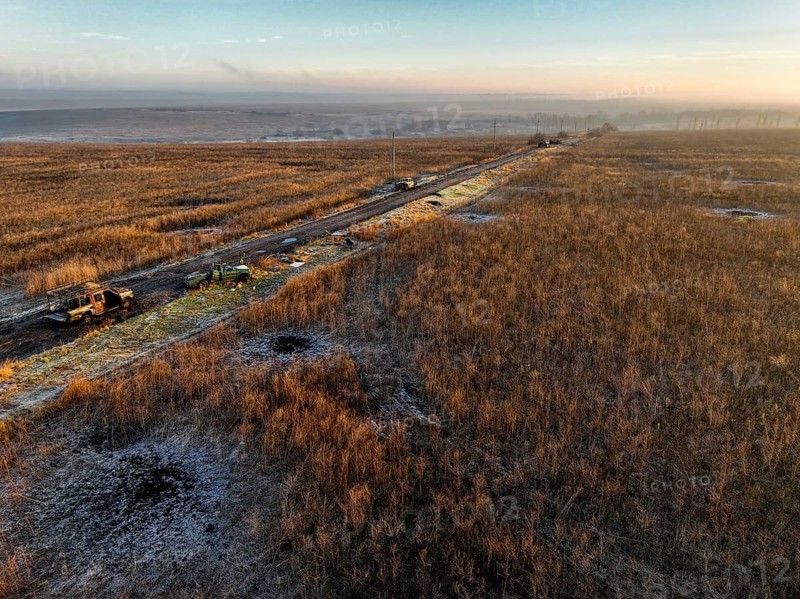 From above, image of military vehicles parked along a rural road impacted by the war through a vast, grassy landscape in Ukraine, showcasing the quiet yet tense atmosphere of the region amidst the ongoing war