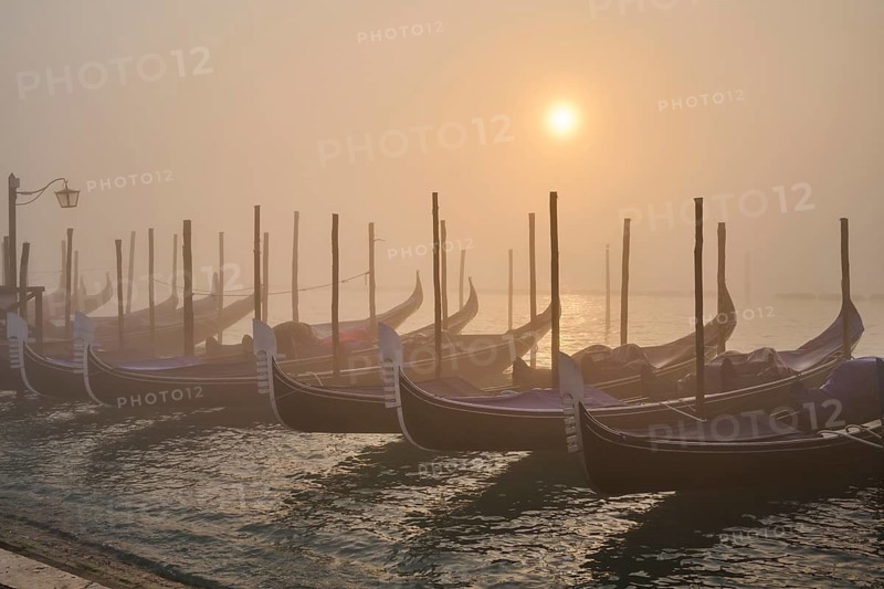 View from 'Colonna di San Marco e San Teodoro' on the gondolas lying in the water at sunrise in Venice on a foggy morning in winter, Italy
