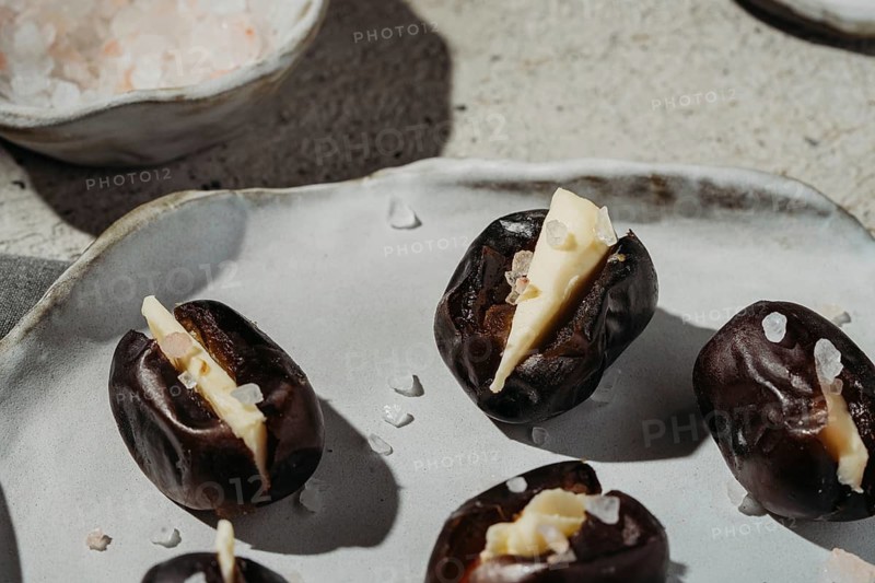 Close-up of butter-stuffed dates sprinkled with sea salt. These sweet and savory treats are elegantly presented on a rustic plate, capturing a gourmet and artisanal feel