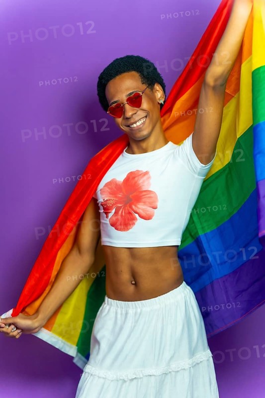 Studio portrait with purple background of a latin transgender person smiling proud and raising lgbt flag