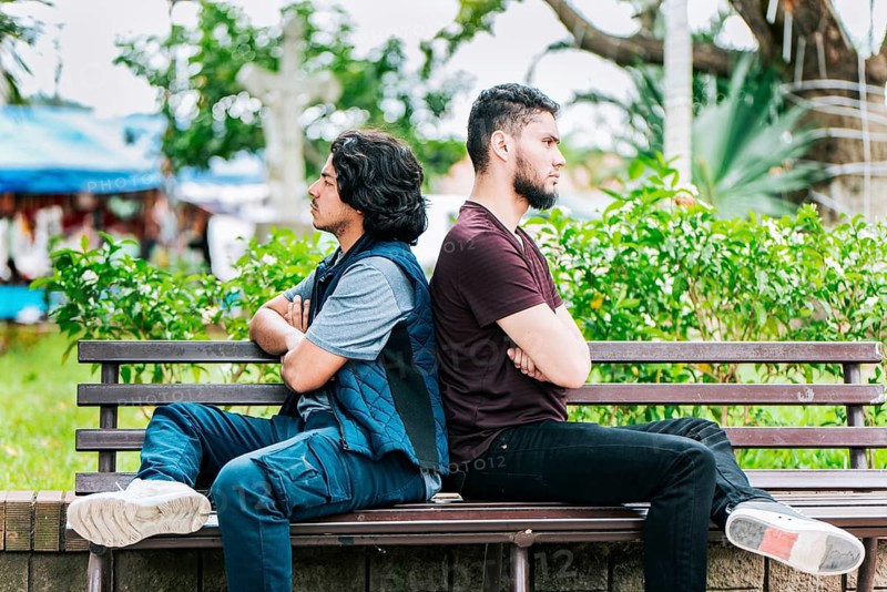 Two friends arguing on a park bench. Two angry friends sitting on a park bench