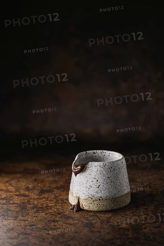 A white speckled ceramic cup with chocolate dripping beautifully down its sides. It is placed on a textured, rustic surface, creating a warm, cozy ambiance