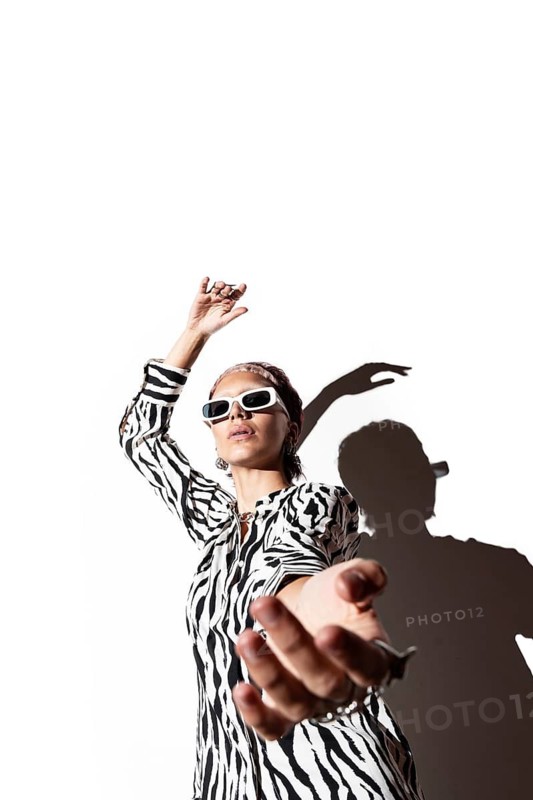 A fashion model in a zebra animal print outfit poses with a dynamic gesture against a stark white background, emphasizing her silhouette with flash photography