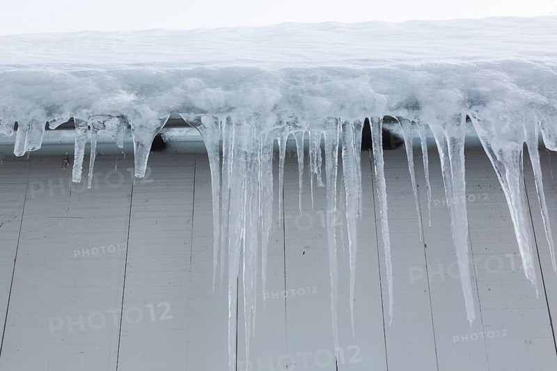 Long icicles and thick heavy ice hanging from roof edge of grey wood plank cladded building in winter, Quebec, Canada