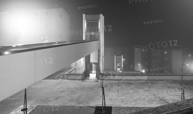 A eerie urban evening captured with a fog enveloped elevator and an overhead walkway connecting modern buildings