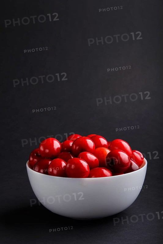 Fresh red sweet cherry in white bowl on black background. side view, copy space