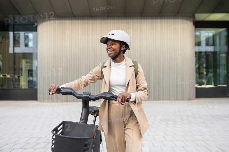 Black woman in a stylish outfit rides an electric bike in a cityscape Helmet on, with a confident smile, symbolizing urban lifestyle and modern mobility