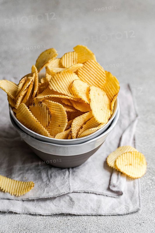 A bowl of crispy homemade potato chips served on a rustic fabric napkin. These golden, wavy chips offer a delicious, crunchy snack perfect for any occasion or gathering