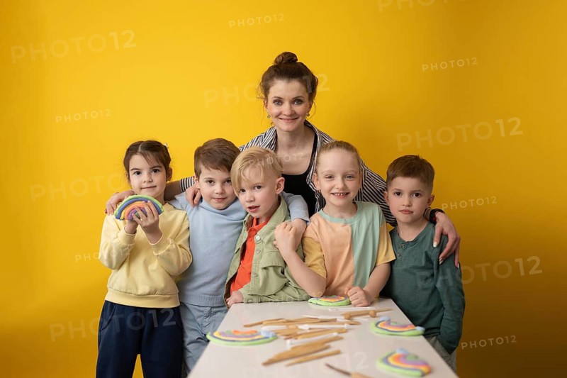 A group of children and their teacher engage in a fun and creative lesson with colorful crafts on a bright yellow background, fostering teamwork and learning