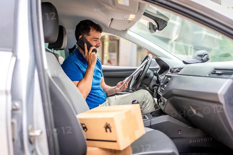 Courier talking to the mobile sitting on a van with packages to deliver