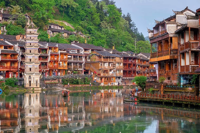 FENGHUANG, CHINA, APRIL 22, 2018: Feng Huang Ancient Town (Phoenix Ancient Town) on Tuo Jiang River with Wanming Pagoda tower and tourist boat on sunset. Hunan Province, China