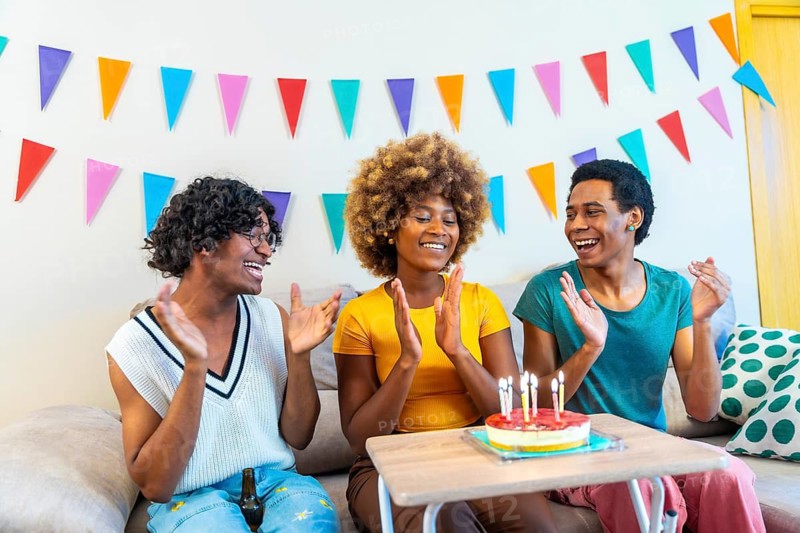 Three multiracial males and female friends singing and clasping hands celebrating birthday at home