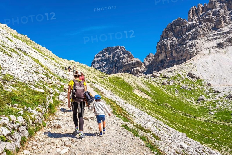 Tourists walking on a scenic mountain trail in the dolomites, enjoying the breathtaking view of the tre cime di lavaredo peaks on a sunny summer day