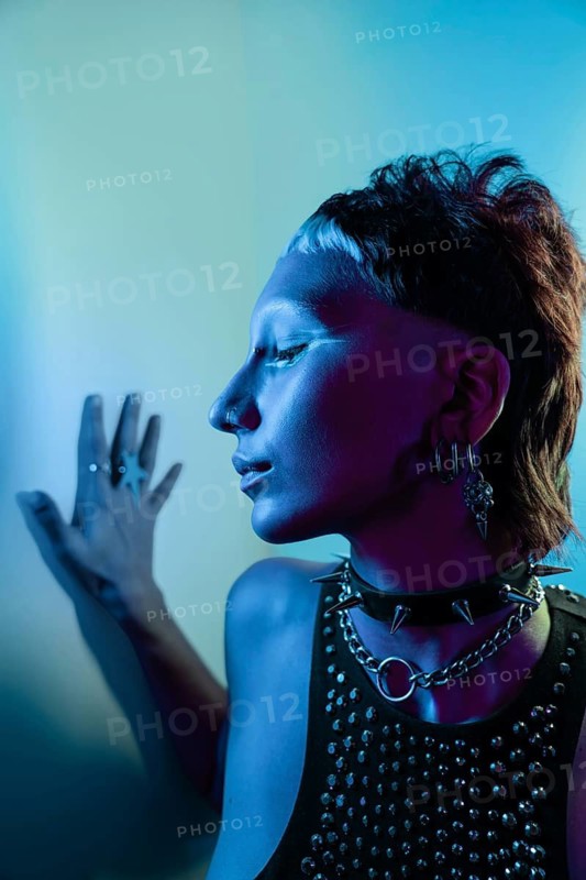 A striking cyberpunk fashion model is captured in vibrant lighting. The edgy look features metallic jewelry, a studded top, and an avant-garde hairstyle, embodying futuristic style