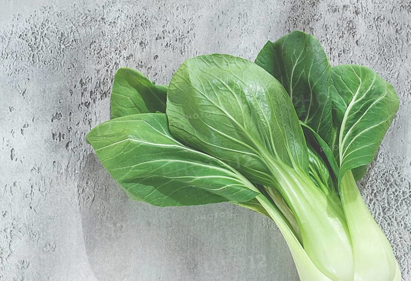 Fresh bok choy, laid out on a light gray surface, top view, natural light