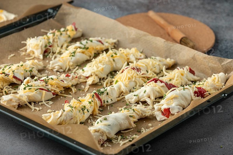 Dough rolls sprinkled with cheese and herbs on baking paper, ready for baking