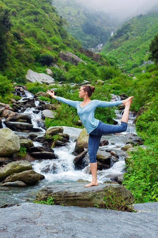 Yoga outdoors, woman doing yoga asana Natarajasana, Lord of the dance balance pose outdoors at waterfall in Himalayas