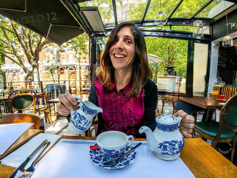 Happy woman pouring milk into her teacup, enjoying a relaxing moment at an outdoor cafe in london
