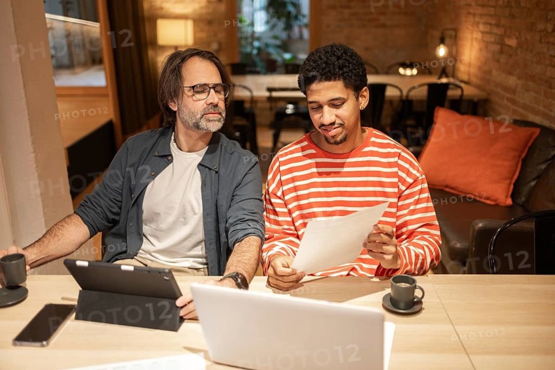 Two professionals collaborate in a cozy coworking space, surrounded by laptops, tablets, and coffee cups, emphasizing teamwork and flexible working environments