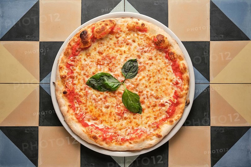 Overhead shot of a classic pizza margherita, featuring melted mozzarella, tomato sauce, and fresh basil leaves, served on a vibrant, geometrically tiled table