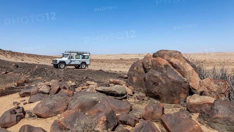 White off-road vehicle in desert-like landscape with large rocks and clear blue sky, Namib-Naukluft National Park near Swakopmund, Namibia