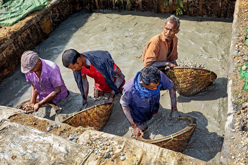 Four men stand in a water-filled area, working with baskets, the sapphire and gemstone mines at Ratnapura in Sri Lanka