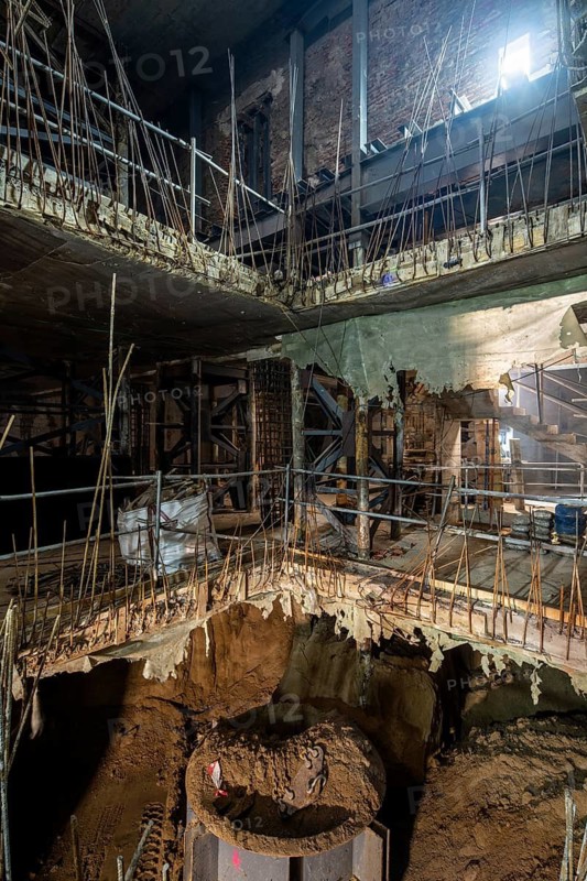 View of an ongoing construction site featuring exposed rebar, concrete floors, and temporary scaffolding, highlighting the structural elements in development