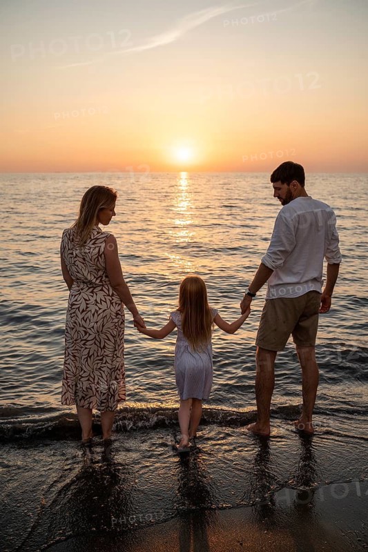A family stands barefoot on the shore of an Italian beach, holding hands as they watch the sun set over the ocean. A peaceful and heartwarming moment filled with love and togetherness