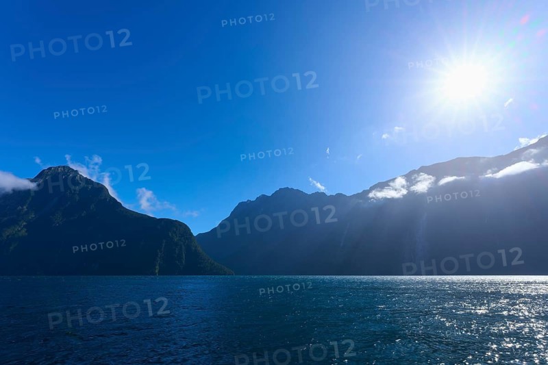 Clear blue fjord landscape with sun over mountains and water, summer, Milford Sound, Te Anau, Fiordland National Park, South Island, New Zealand