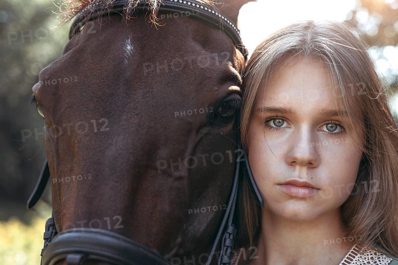 Close up portrait of a young girl beside a brown horse, capturing a serene moment in a natural setting. The sunlight adds a warm glow to their expressions
