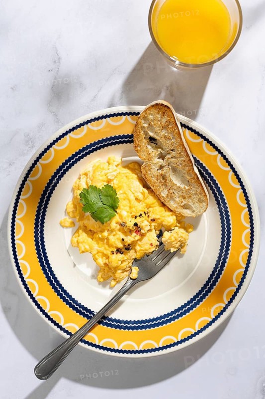 A colorful breakfast setting featuring fluffy scrambled eggs garnished with herbs, served with a slice of toasted bread and a refreshing glass of orange juice